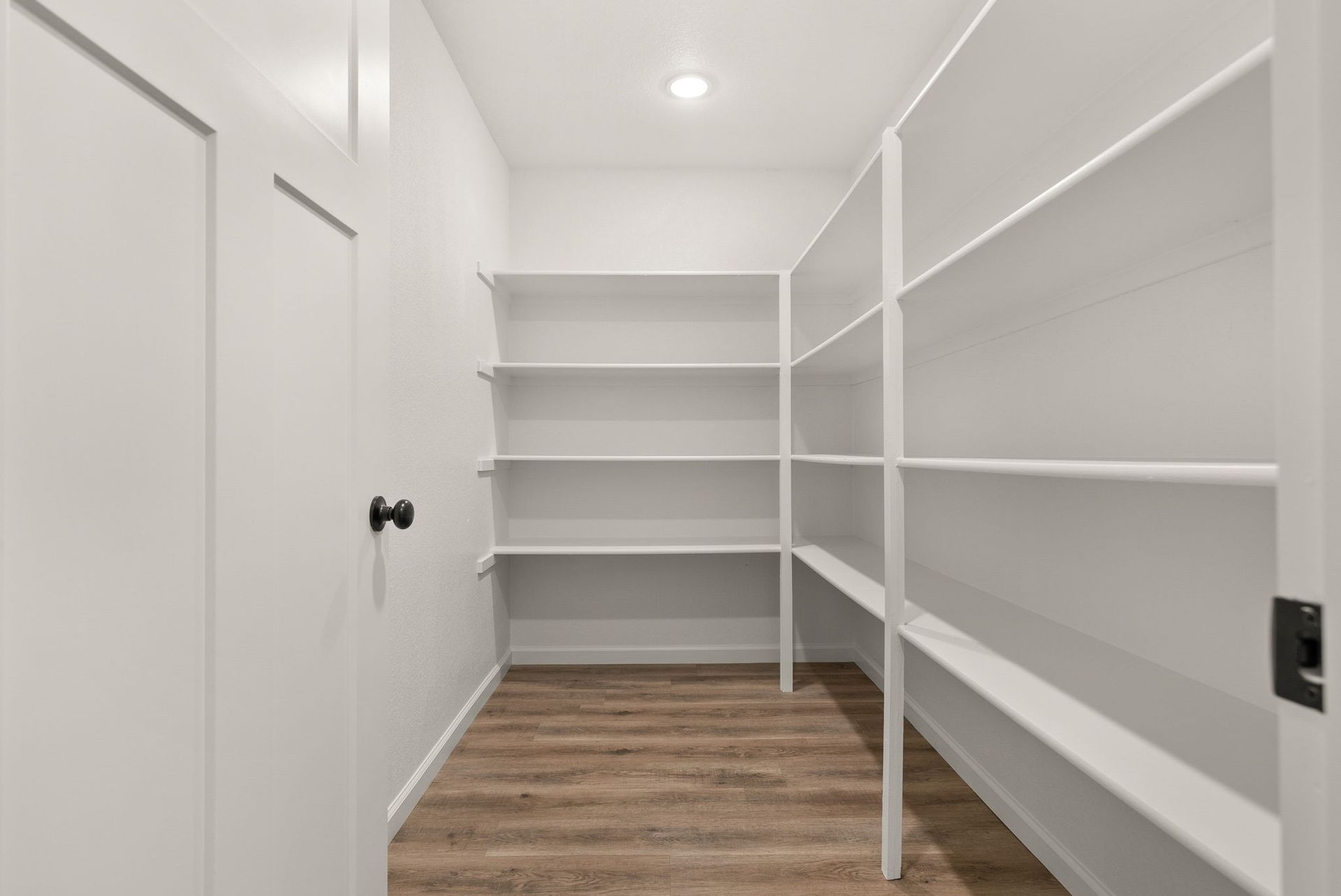 A walk in closet with wooden floors and white shelves.