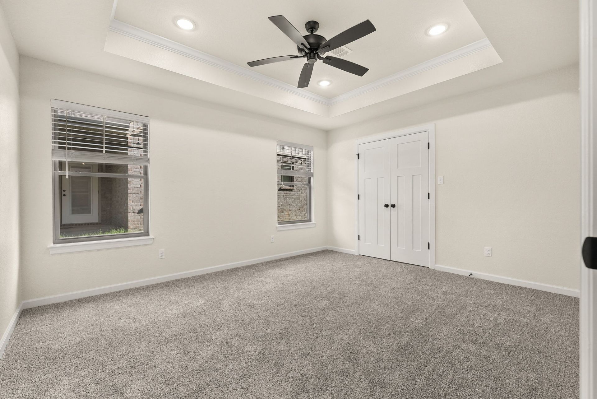 An empty bedroom with a ceiling fan and two windows.