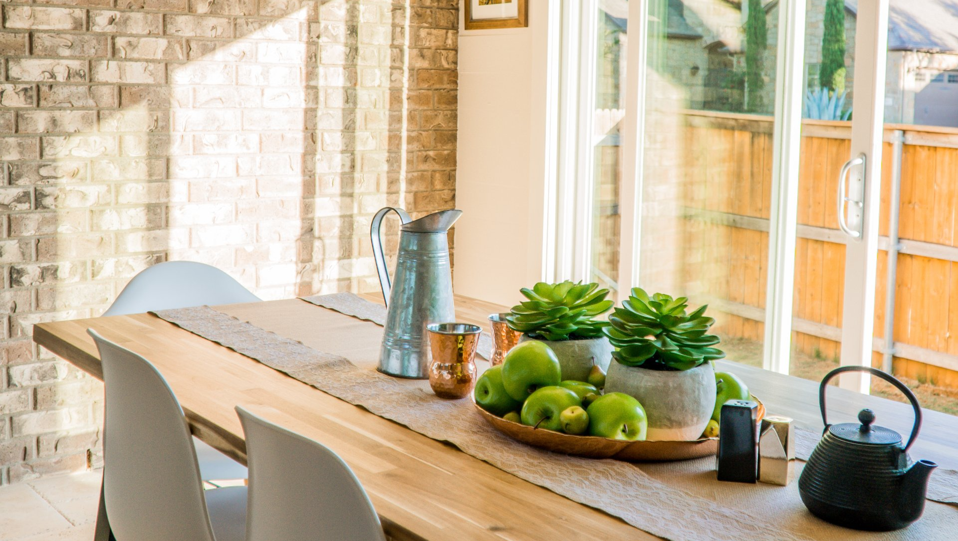 A dining room table with a bowl of apples and potted plants on it.