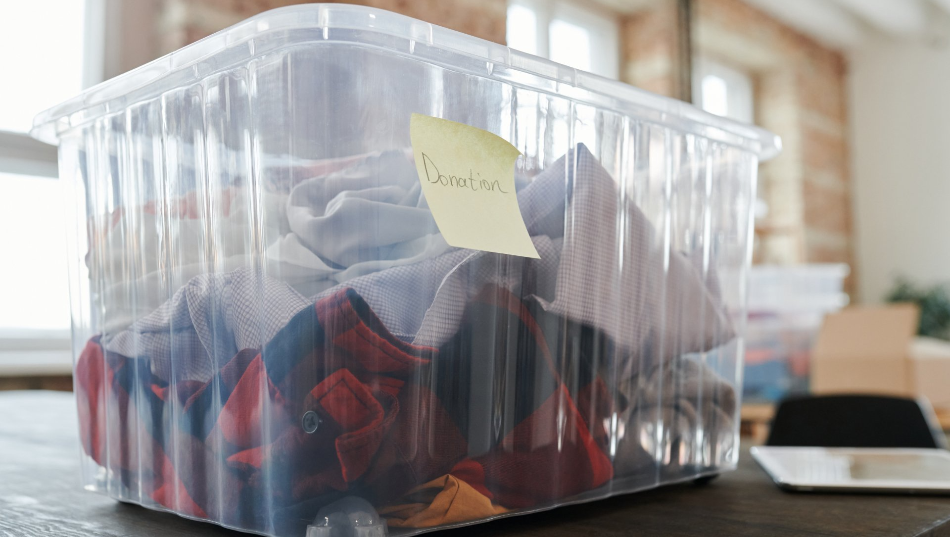 A clear plastic bin filled with clothes and a sticky note on it.