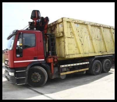 Camion rosso con cassone ribaltabile giallo, visto di profilo su una superficie di cemento.