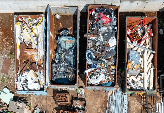 Veduta aerea di quattro grandi cassonetti pieni di detriti misti da costruzione e metallici in un cantiere.