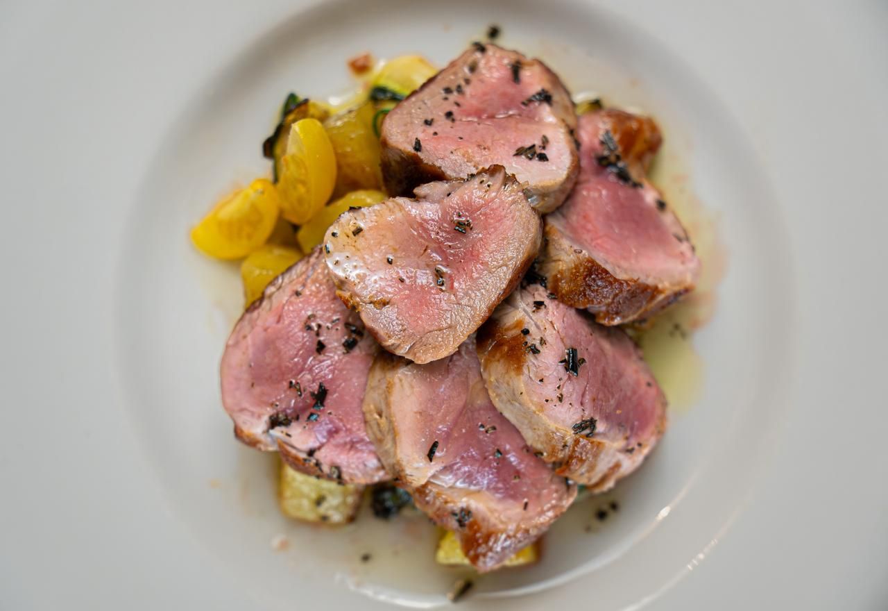 Arrosto di carne rosa affettato, con erbe aromatiche, su un piatto bianco, servito con verdure gialle.