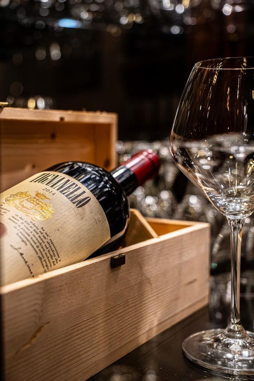 Bottiglia di vino in una scatola di legno accanto a un bicchiere su un tavolo poco illuminato