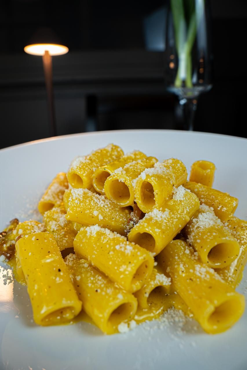 Rigatoni impiattati con formaggio grattugiato, in un ristorante dall’atmosfera soffusa