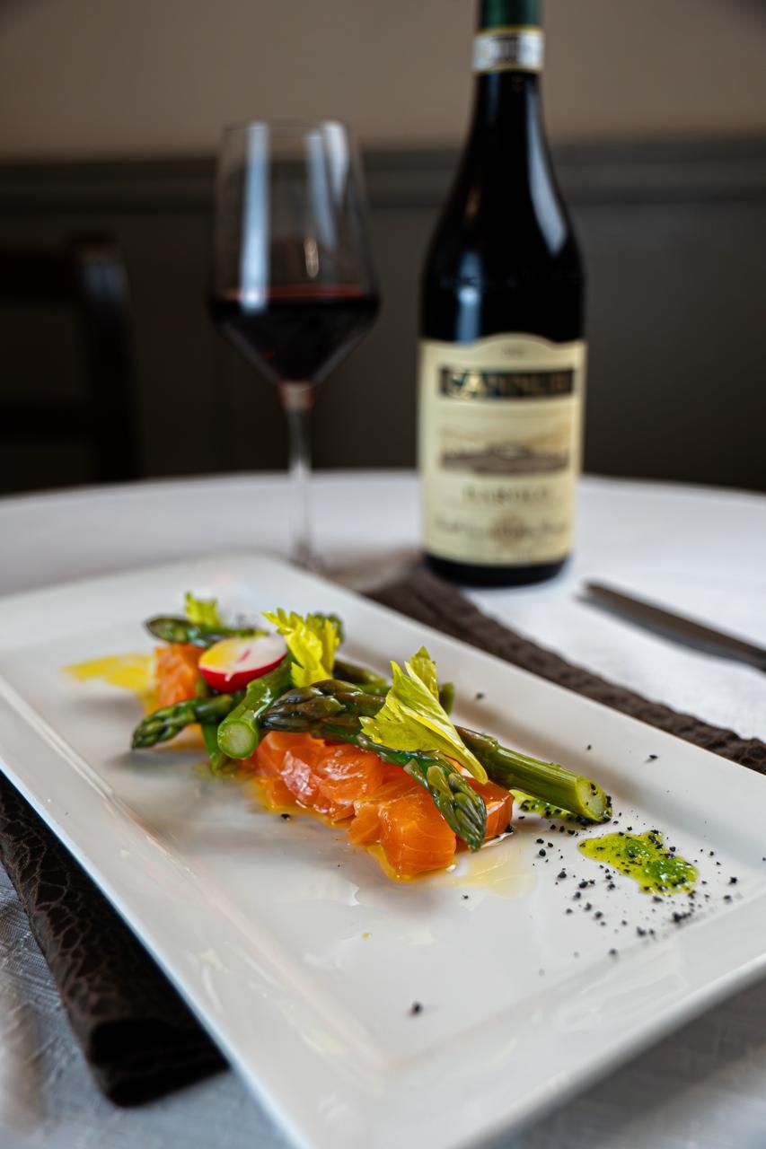 Piatto gourmet di salmone impiattato con verdure e vino su una tovaglia bianca