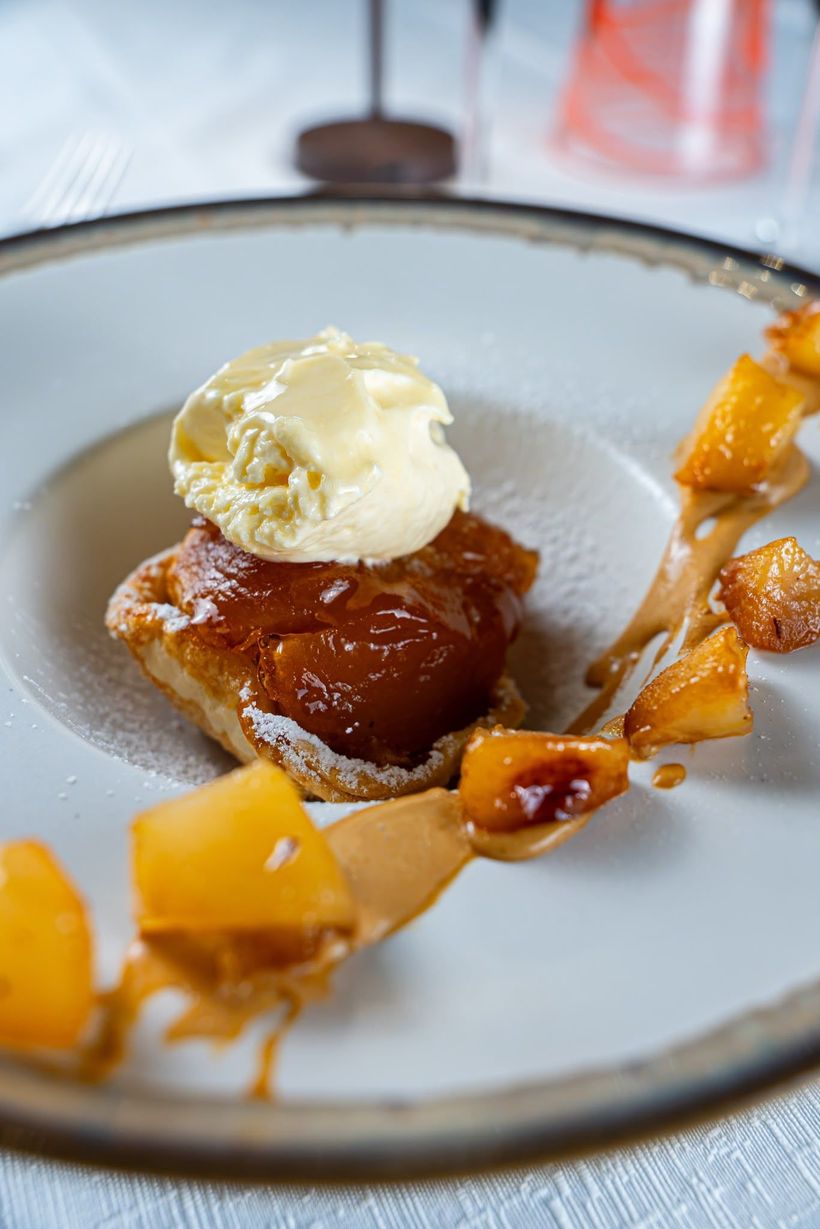 Piatto da dessert con dolce ricoperto di caramello, una pallina di gelato alla vaniglia e salsa al mango a filo