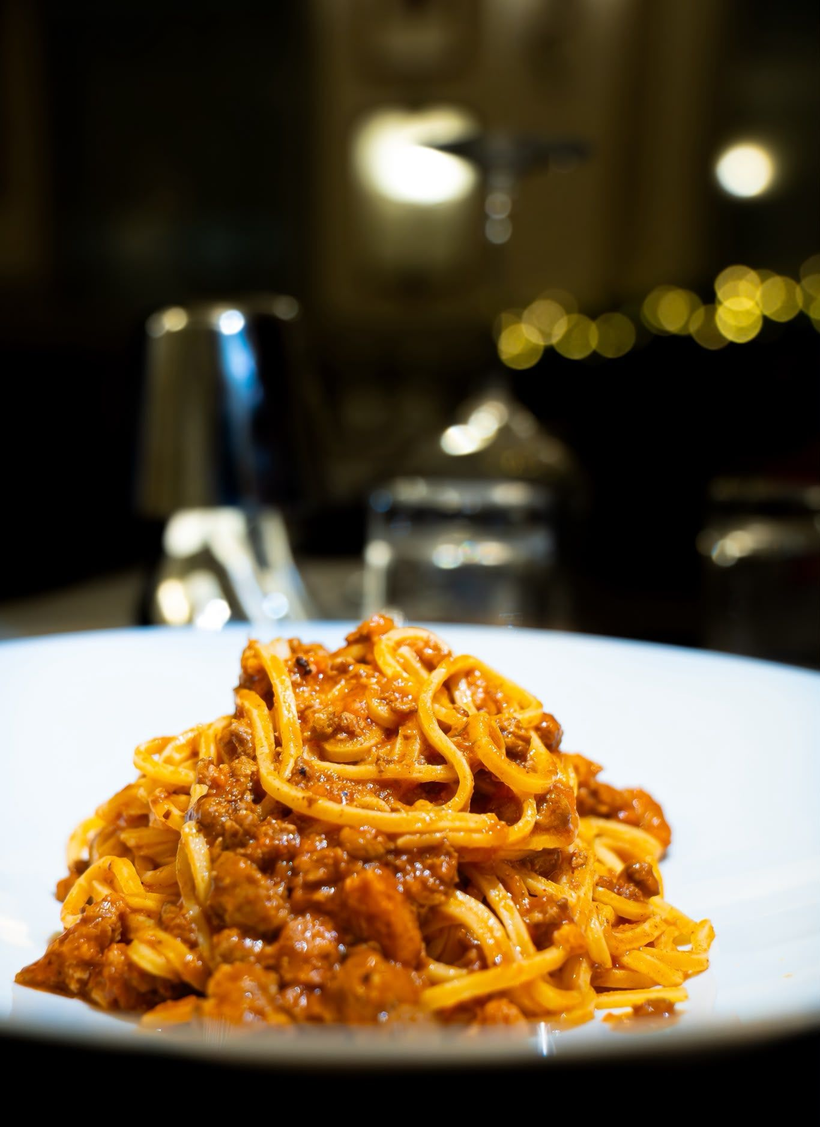 Piatto di spaghetti al ragù su un tavolo, con le luci sfocate di un ristorante sullo sfondo