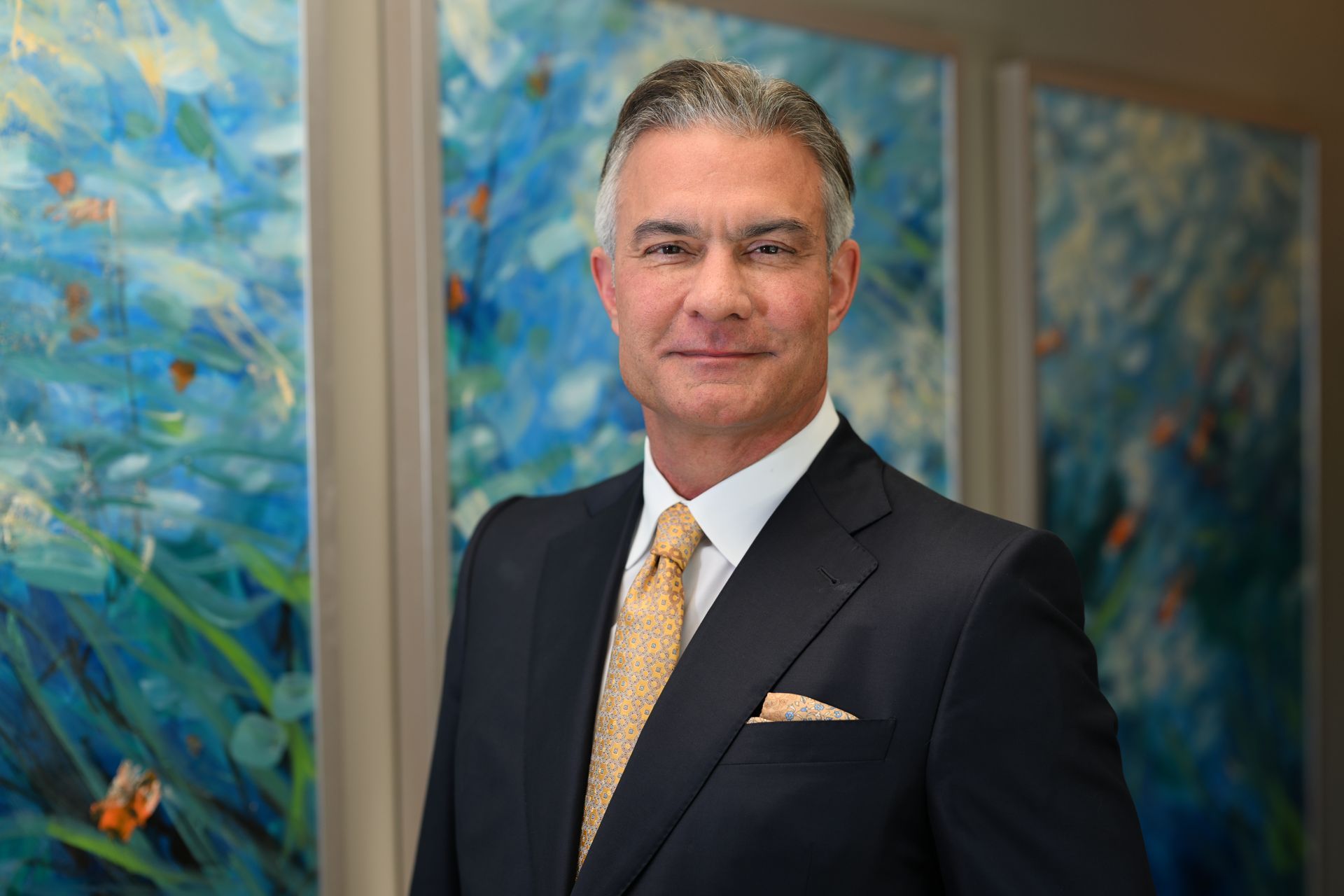 Man in suit, smiling, in front of abstract blue and white artwork.