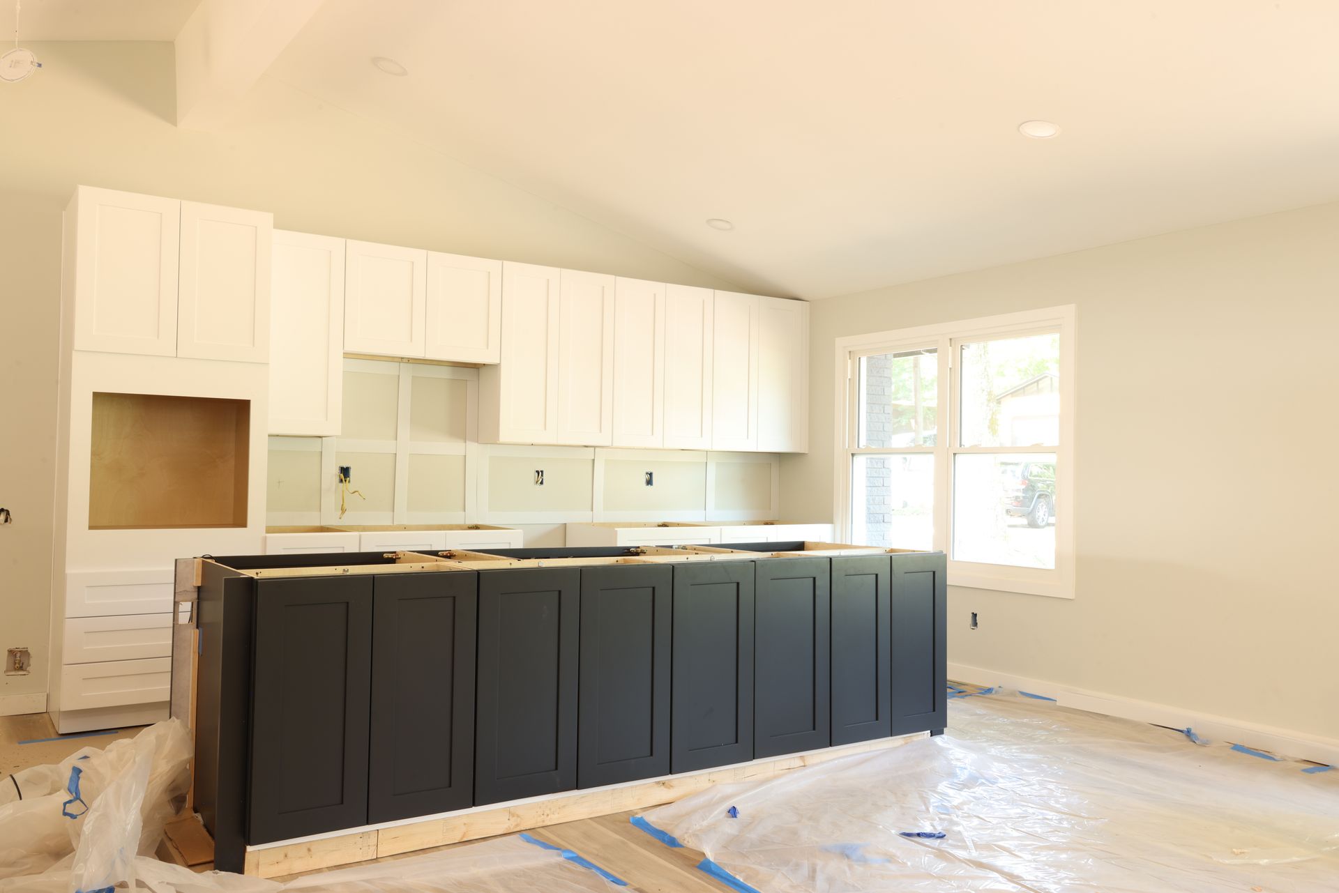 A kitchen under construction featuring white upper cabinets, a dark charcoal island, and drop cloths on the floor.