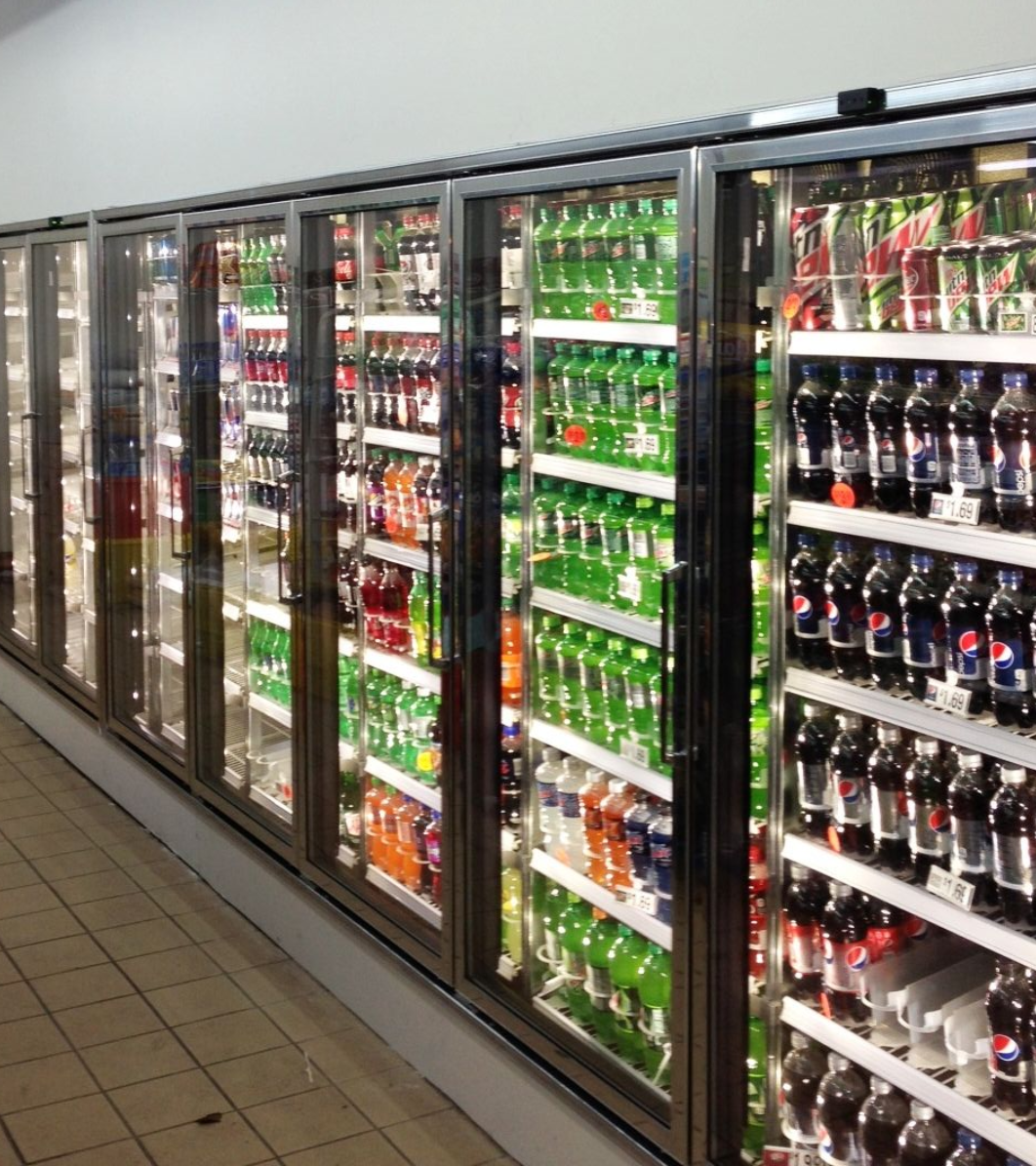 An angled, high-angle view of a long row of glass-doored supermarket refrigerators filled with rows of bottled beverages.