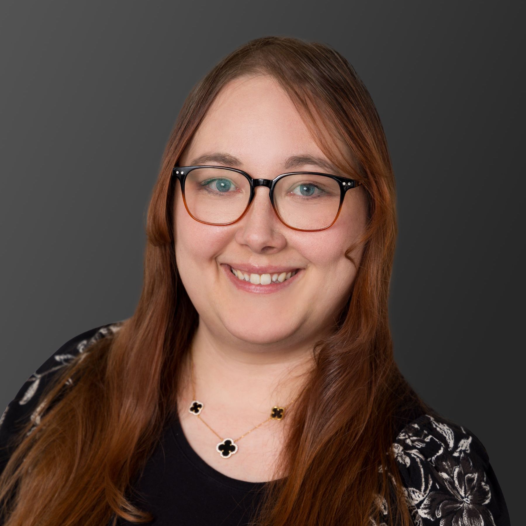A woman wearing glasses and a necklace is smiling for the camera.