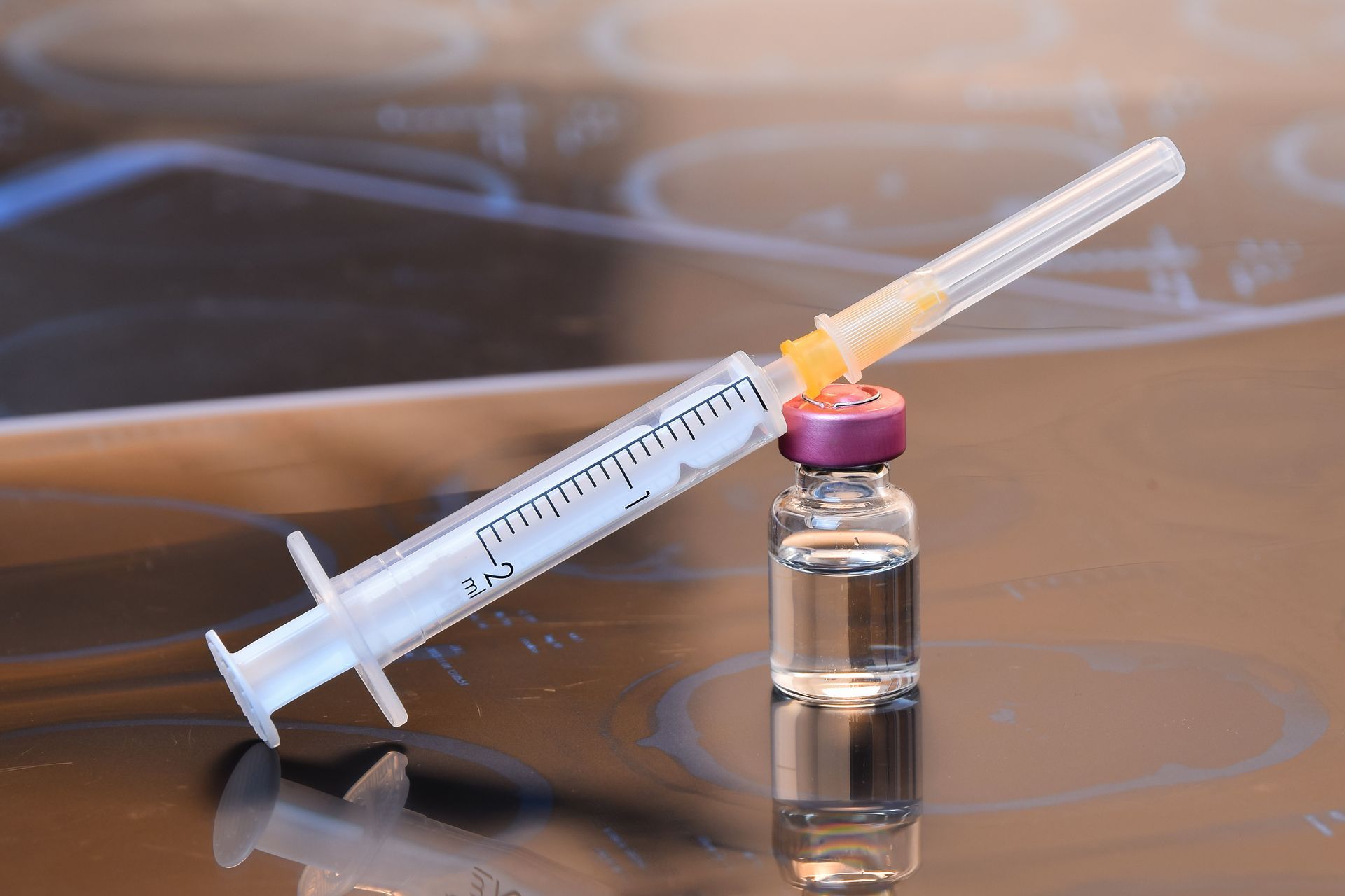 Syringe with yellow liquid leaning against a small vial on a brown surface