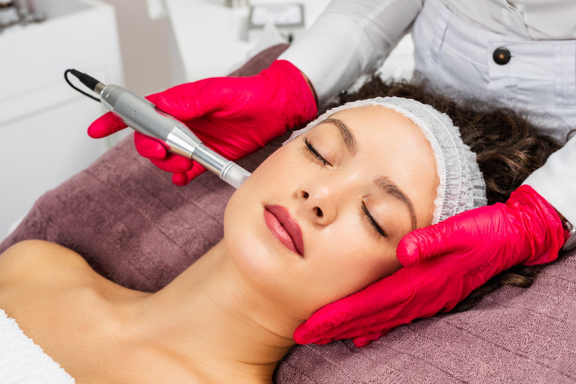 Facial treatment with a device on a relaxed client wearing a headband and red gloves in a spa room
