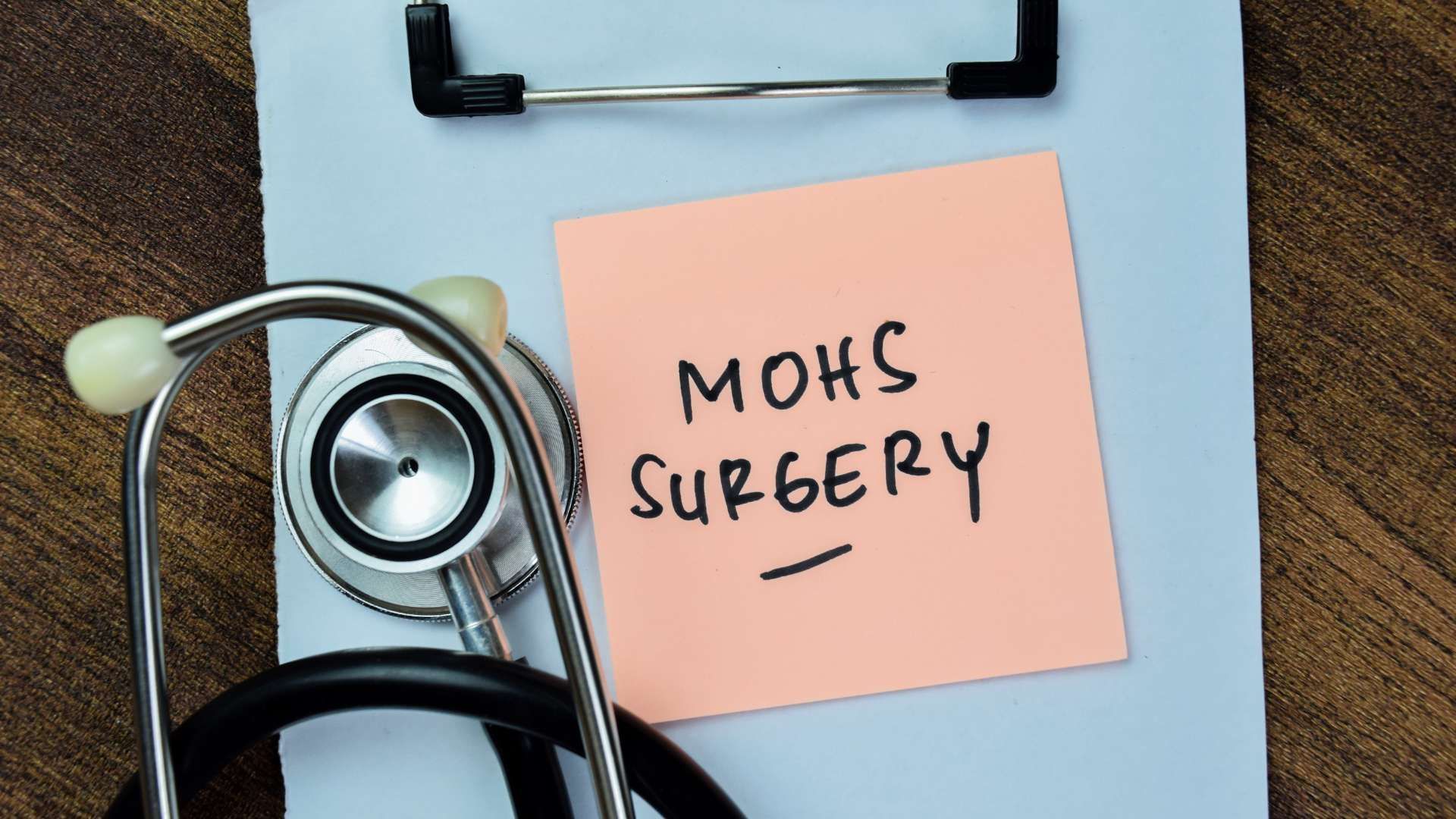 Stethoscope beside a pink note labeled “Mouth Surgery” on a clipboard with blue paper.