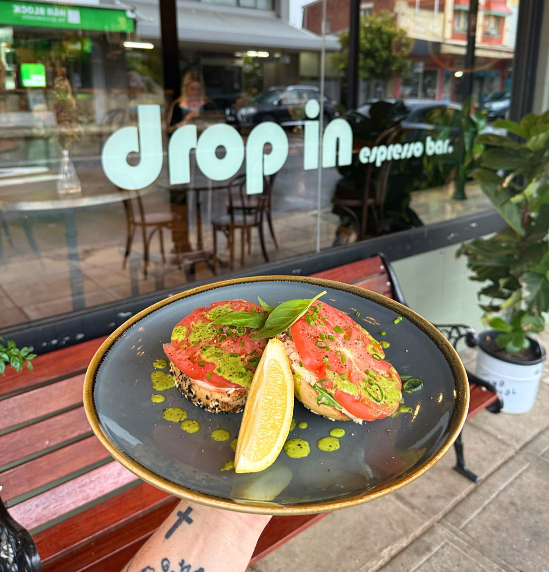 Plate of food with tomato, pesto, and lemon held in front of a coffee shop window  — Drop In Espresso Bar in Wallsend, NSW 