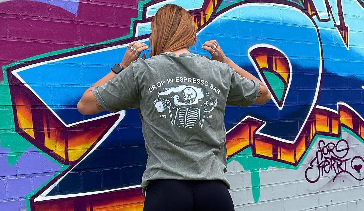 Person in green shirt with graphic, standing in front of graffiti wall — Drop In Espresso Bar in Wallsend, NSW