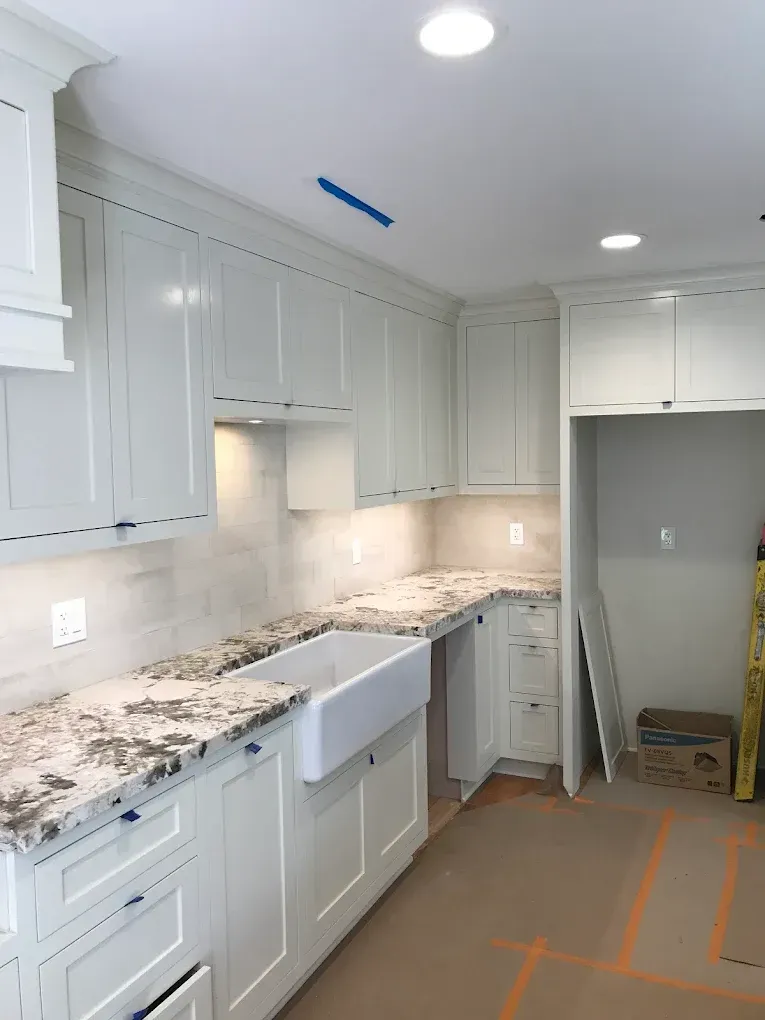 White kitchen cabinets with granite countertops, under-cabinet lighting, and a farmhouse sink.