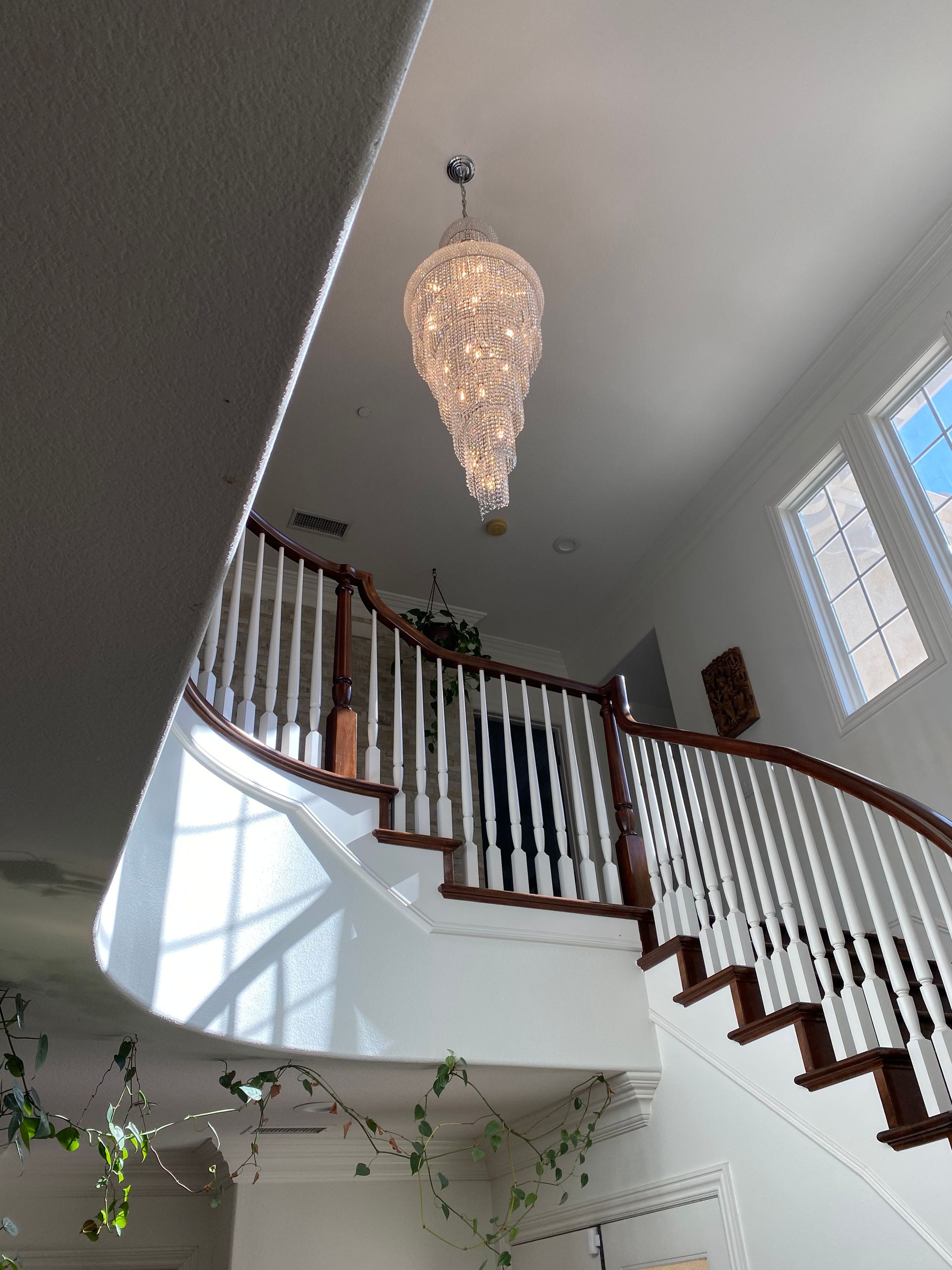 A grand staircase with white railings, wooden steps, and a chandelier hanging from the high ceiling.