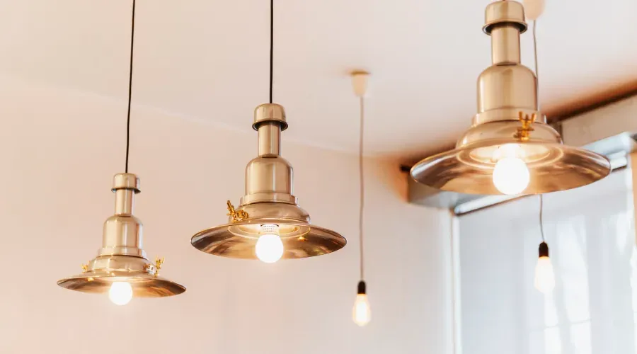Three metallic pendant lights hanging from a white ceiling, lit bulbs.