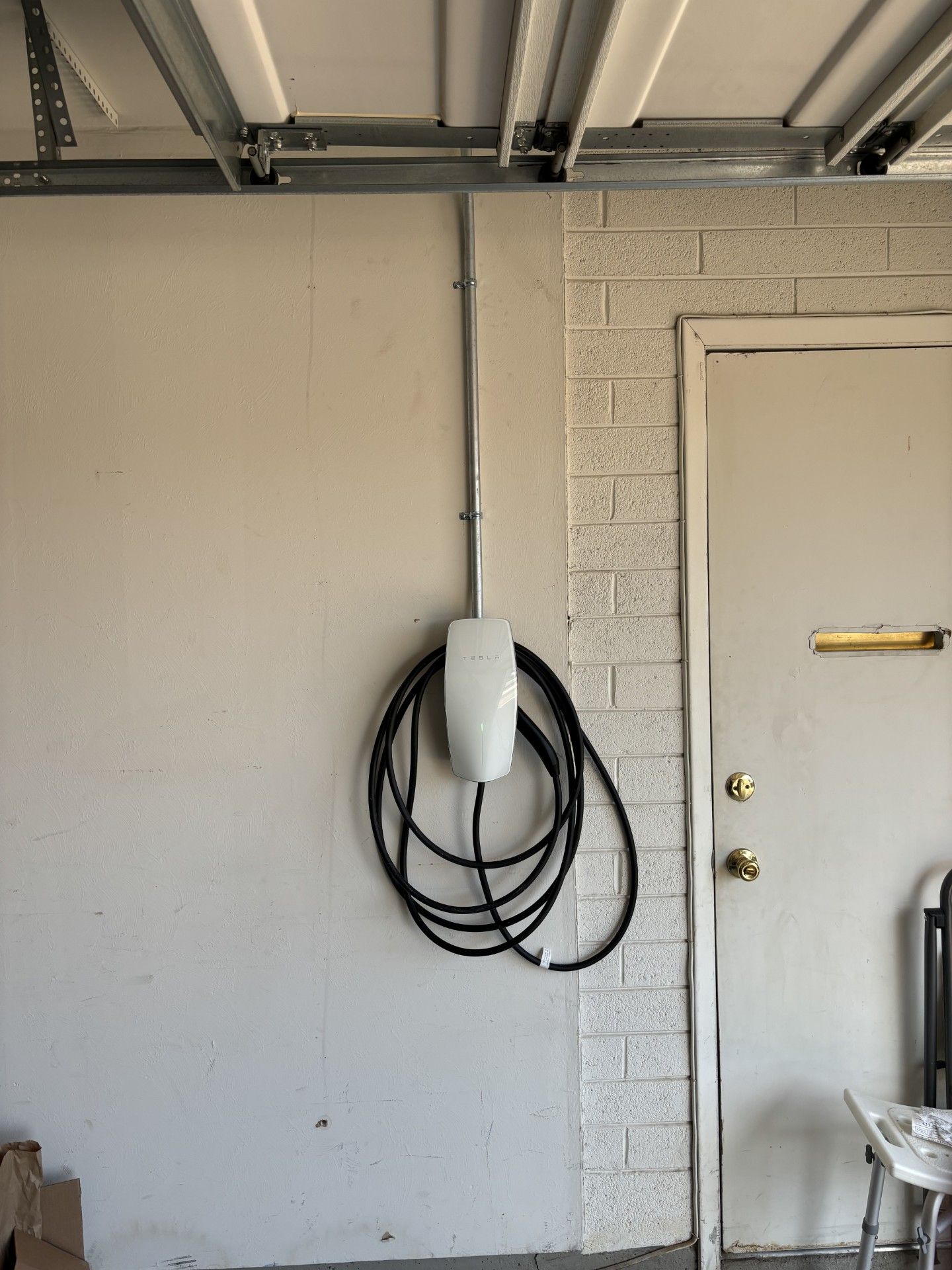 White electric vehicle charger mounted on a garage wall with a coiled black cable.