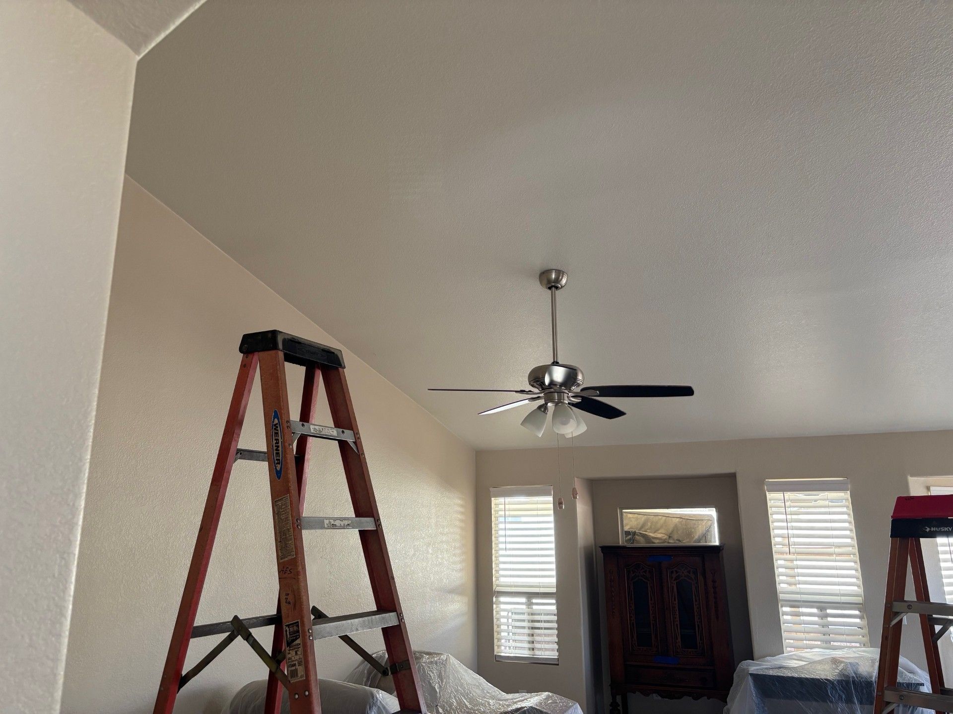 A-frame ladder next to a wall, reaching towards a ceiling with a ceiling fan.
