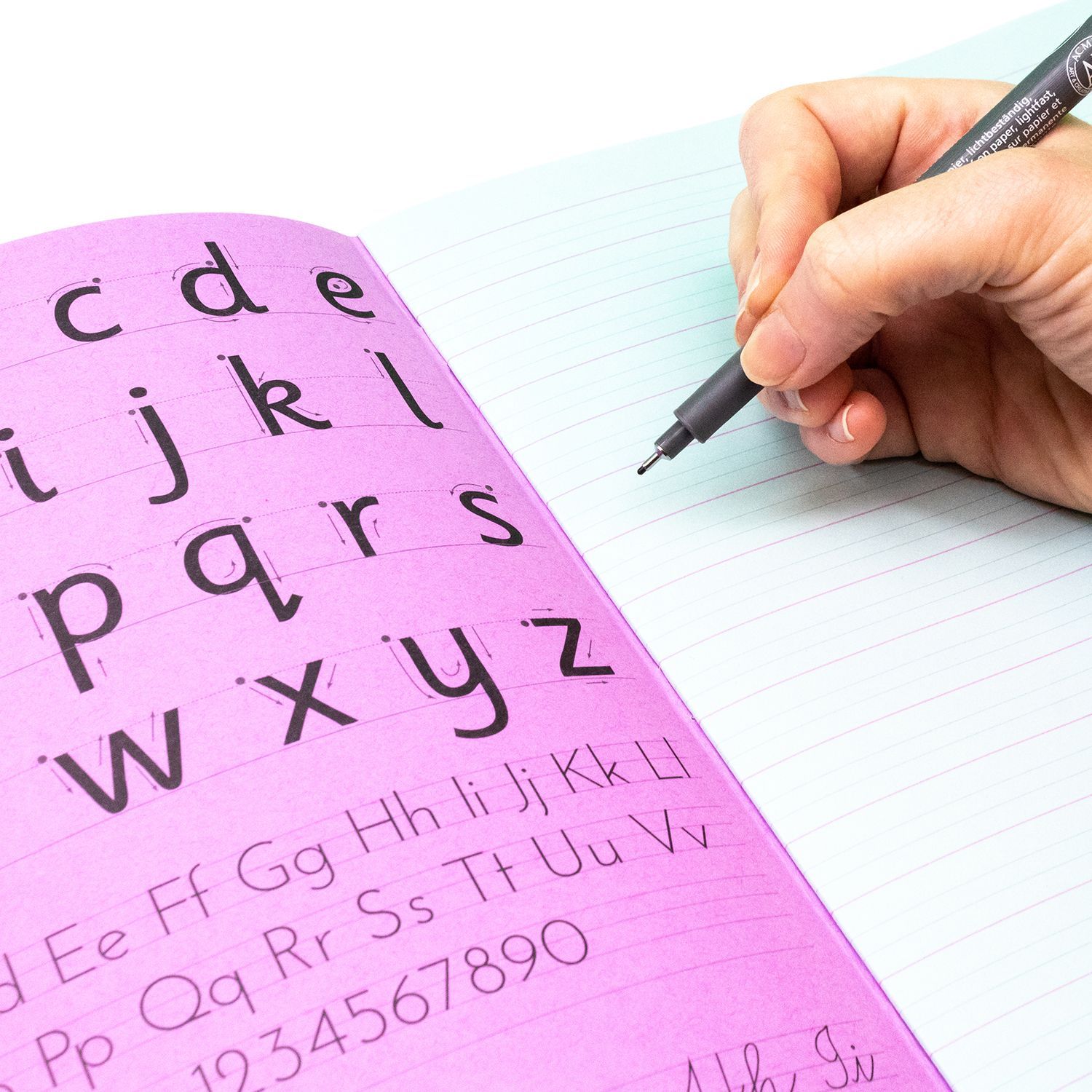 Silvine Sense Handwriting book in use. The book is open to reveal the blue tinted paper and alphabet inner cover, with a hand holding a pen, poised and ready to write.
