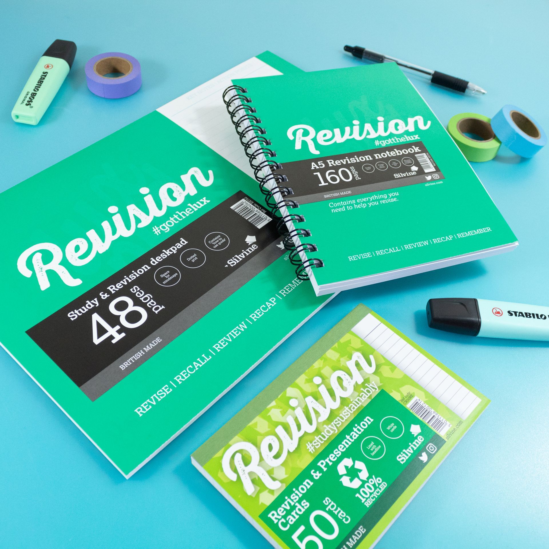 Silvine revision cards, notebook and desk pad on blue background with stationery items around