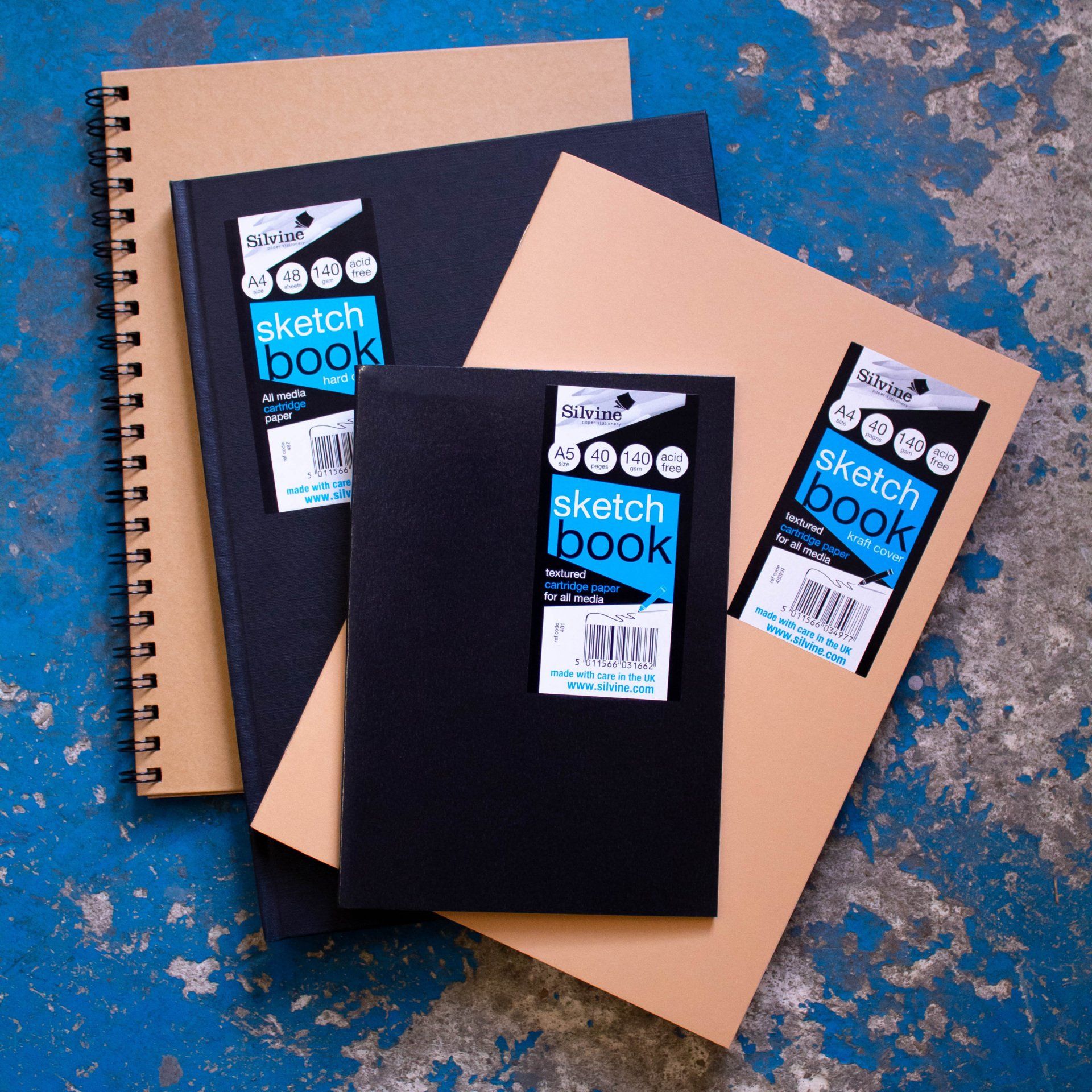 Four sketchbooks by Silvine - both black and kraft covers, on a blue distressed background.