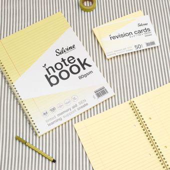 Yellow tinted notebook, revision card pack and yellow stationery accessories on a grey lined background.