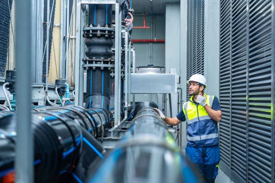 Technicien portant casque et gilet de sécurité inspectant des canalisations industrielles dans un couloir d'usine