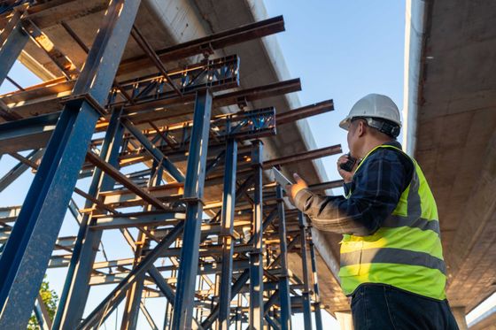 Un ouvrier du bâtiment, portant un casque et un gilet réfléchissant, inspecte un échafaudage sur un chantier.