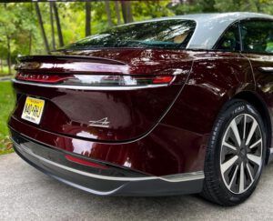 Maroon sedan viewed from the rear, parked on a tree-lined road.