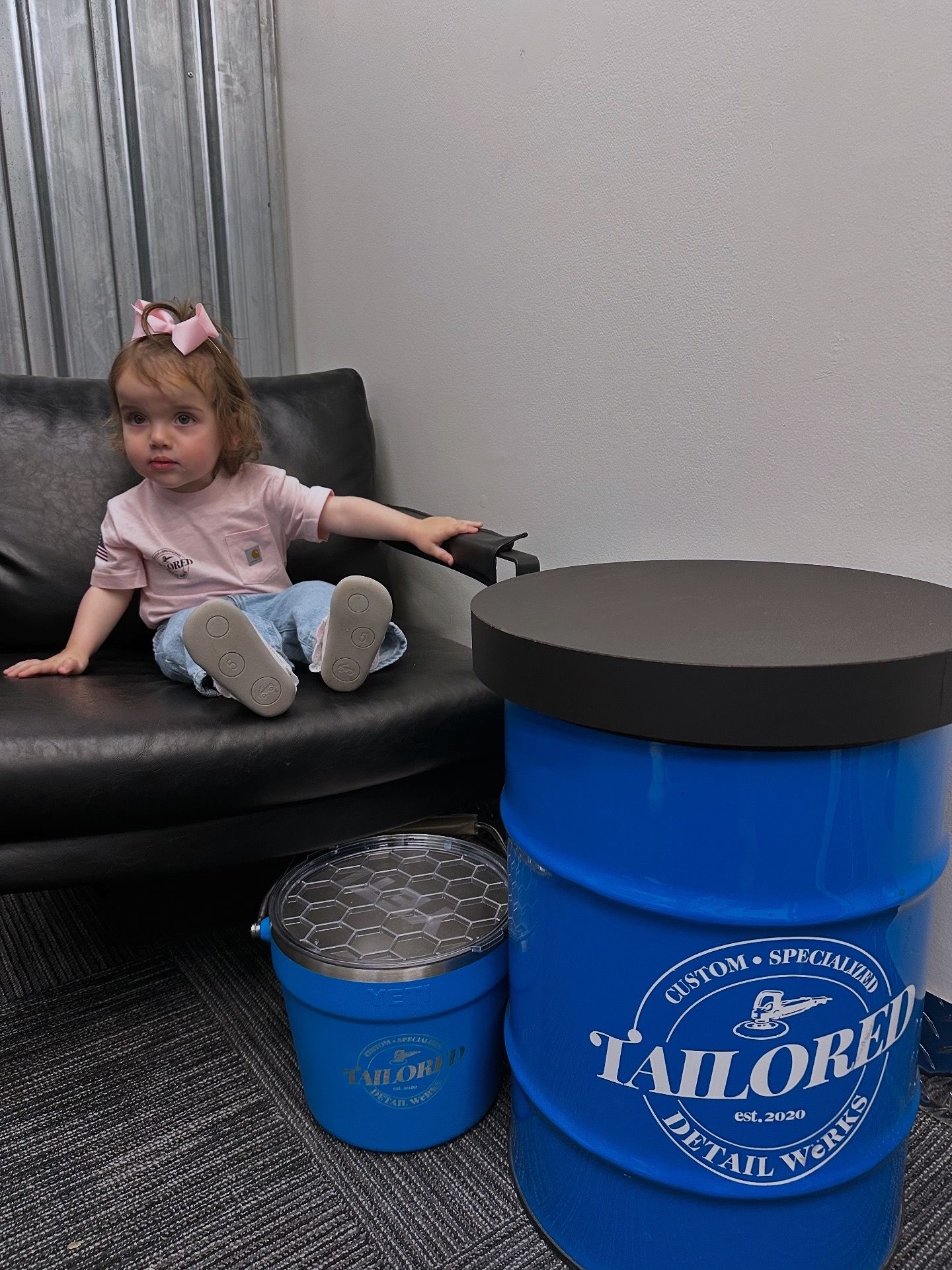 Toddler sitting on a black couch beside blue and black barrel-shaped tables in a gray room.