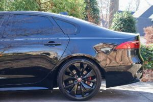 Black sedan parked outdoors with tinted windows and black rims, seen from the side.