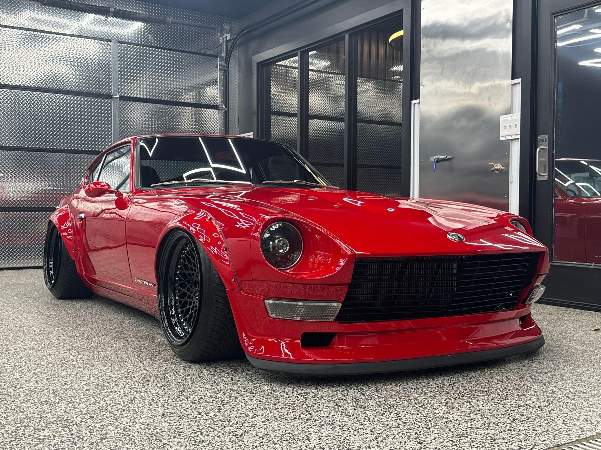 Red classic sports car in a garage, low-angle front view, glossy finish and black wheels.