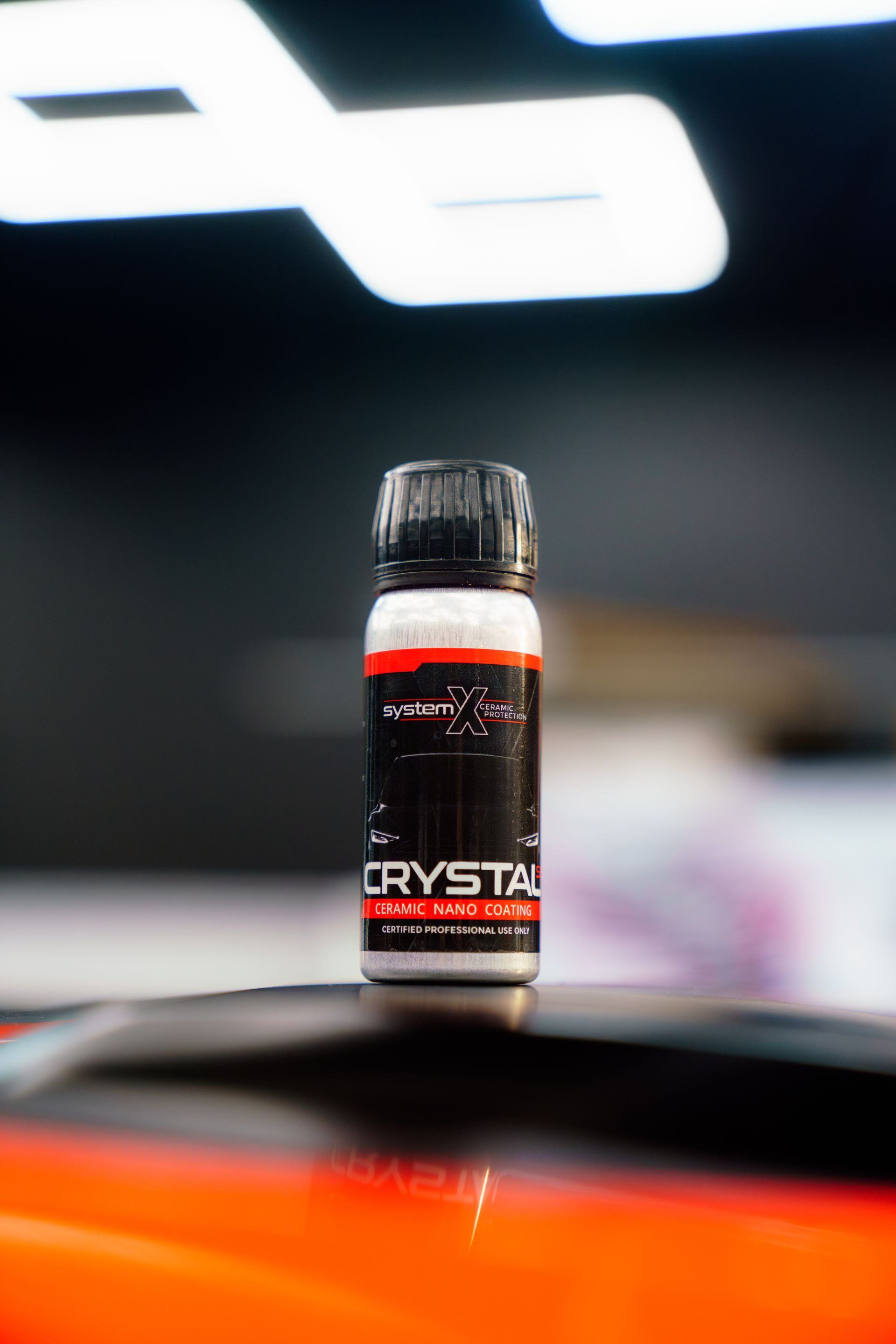 Small black bottle with red label on a car hood, blurred garage background