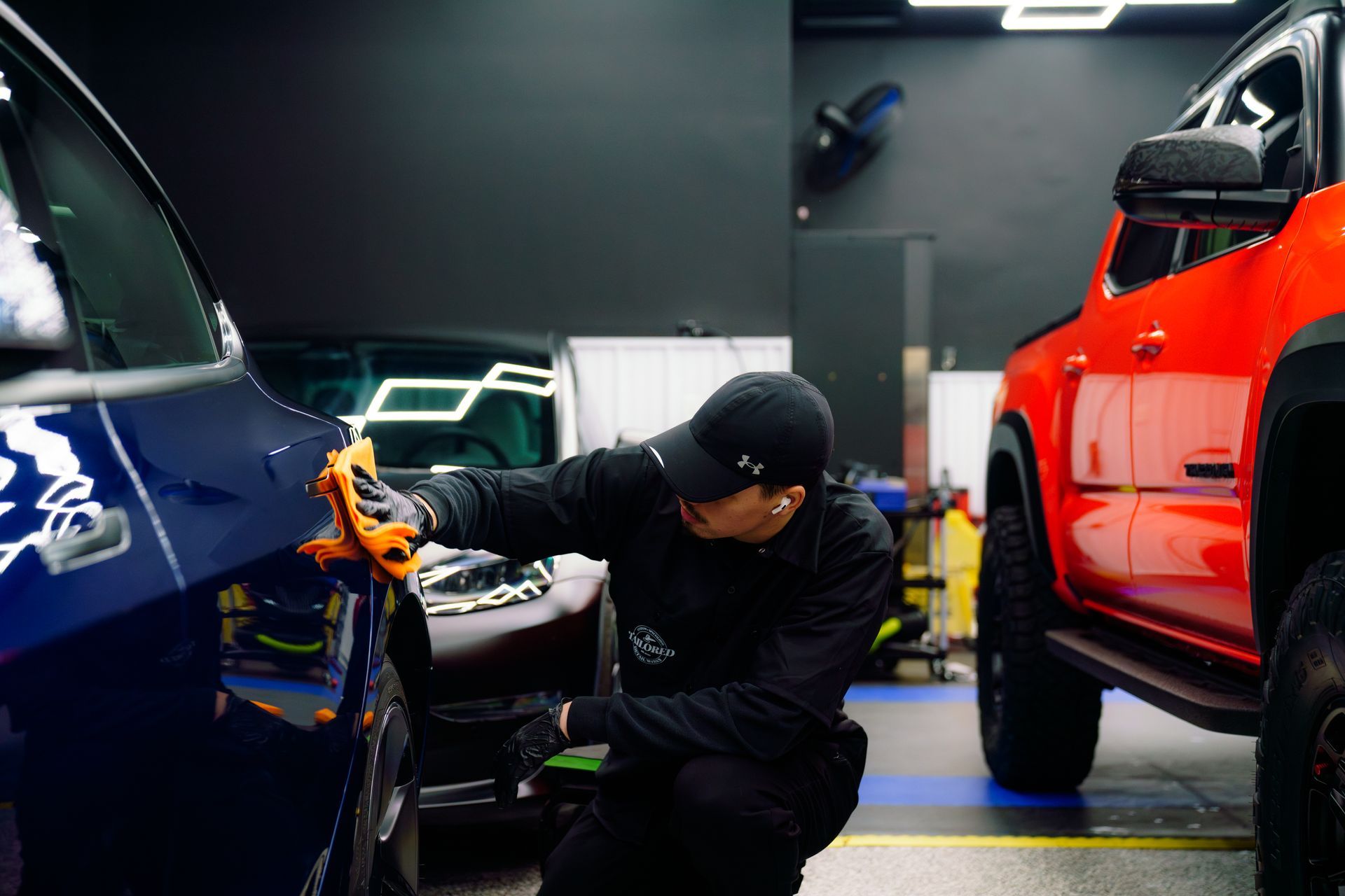 Person polishing a blue car beside a red SUV in a garage