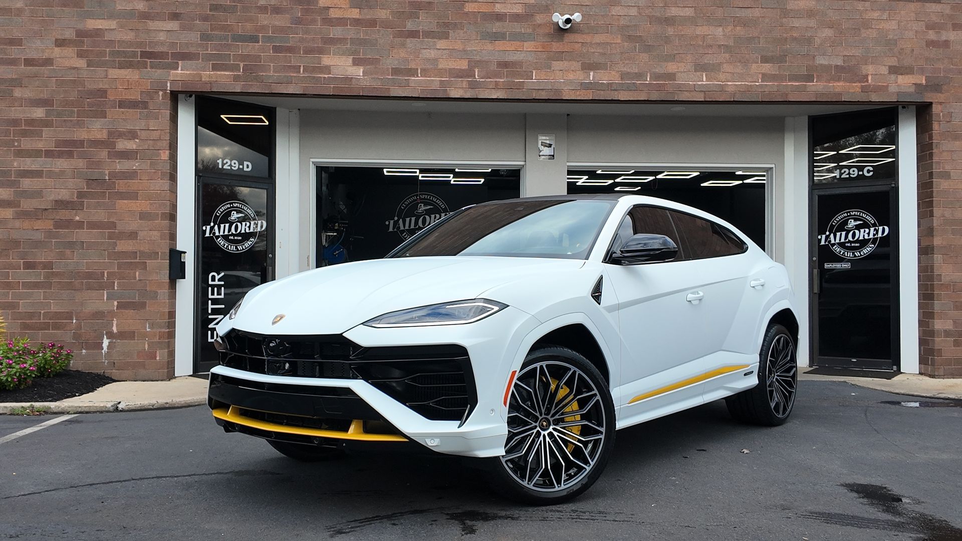 White Lamborghini Urus parked outside a brick storefront, front three-quarter view