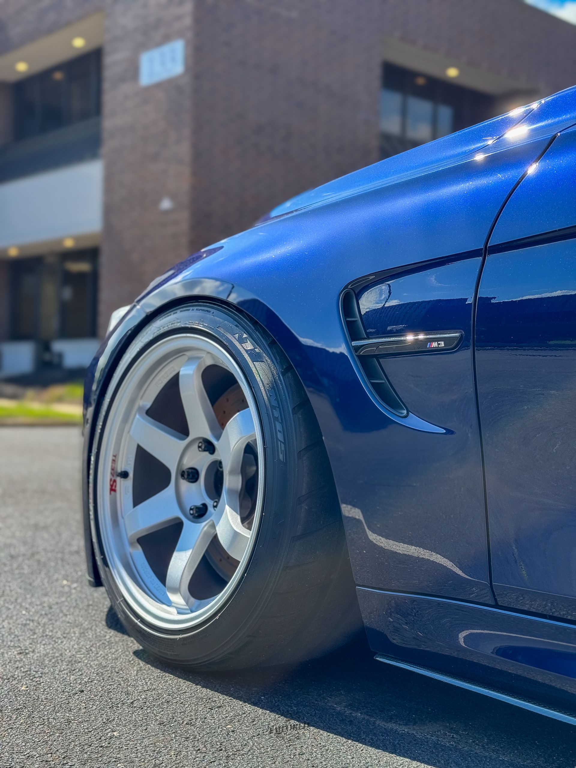 Low blue sports car with polished silver wheel and stretched tire parked outside a building