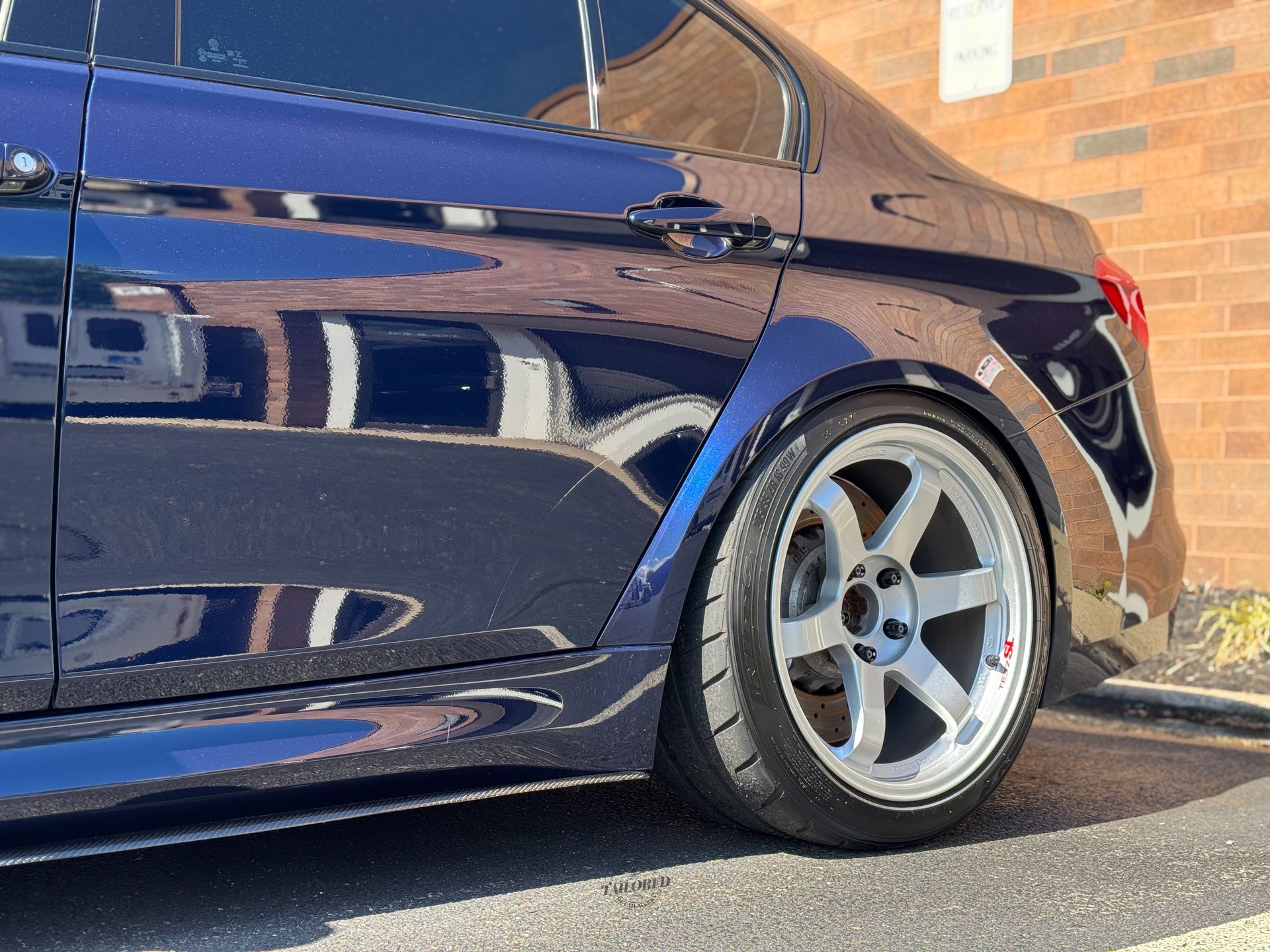 Dark blue car with silver alloy wheel parked on pavement, close-up side view