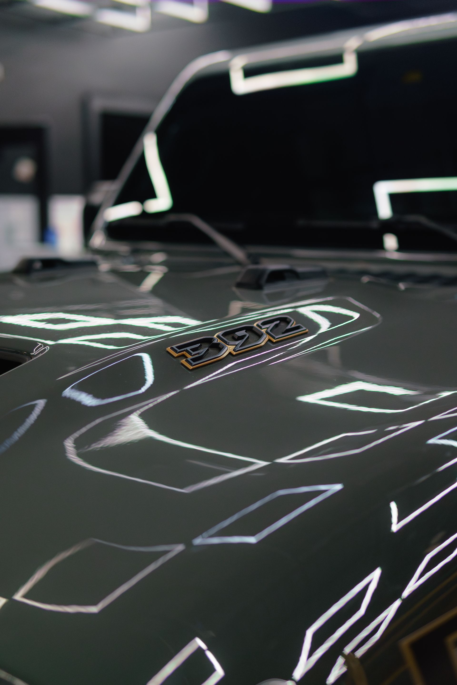Close-up of a glossy black car hood with reflective white light patterns in a dim garage.