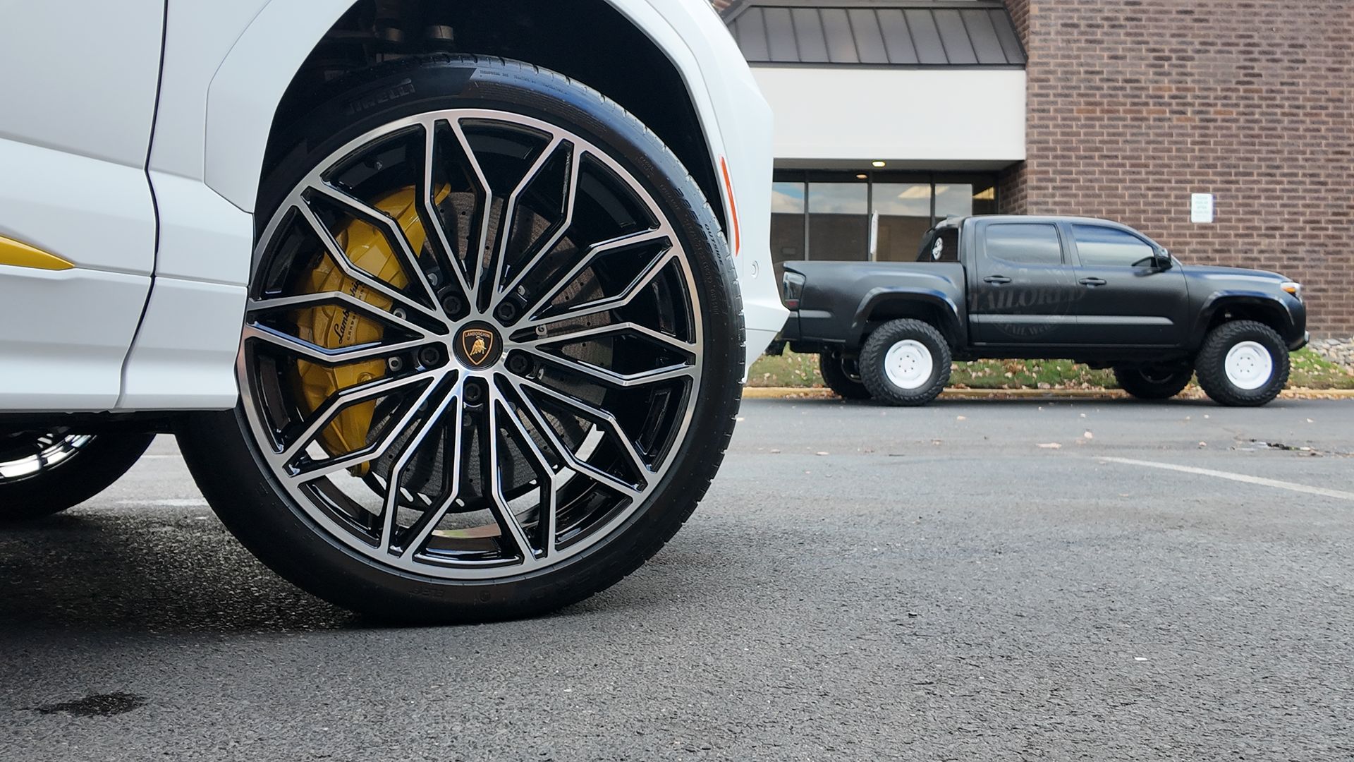 Close-up of a white truck’s black alloy wheel with yellow brake caliper, parked near a black pickup.