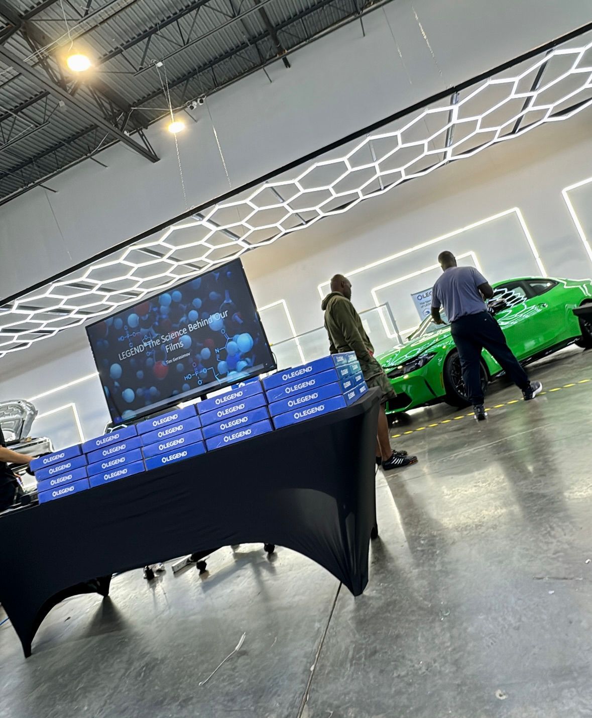 Indoor showroom with blue-lit display table, two people, and a bright green sports car in the background