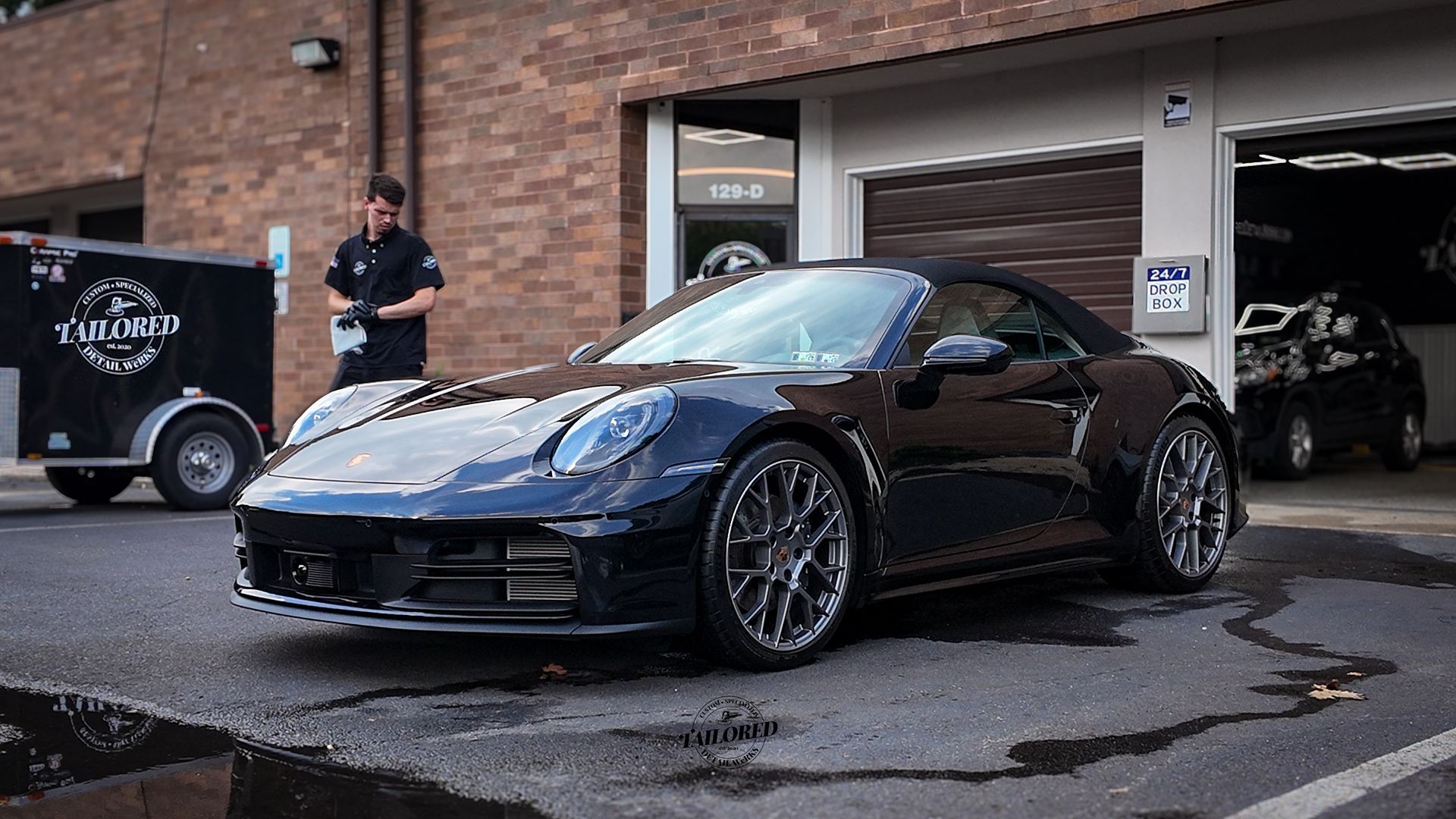 Black sports car parked outside a garage with a person standing nearby