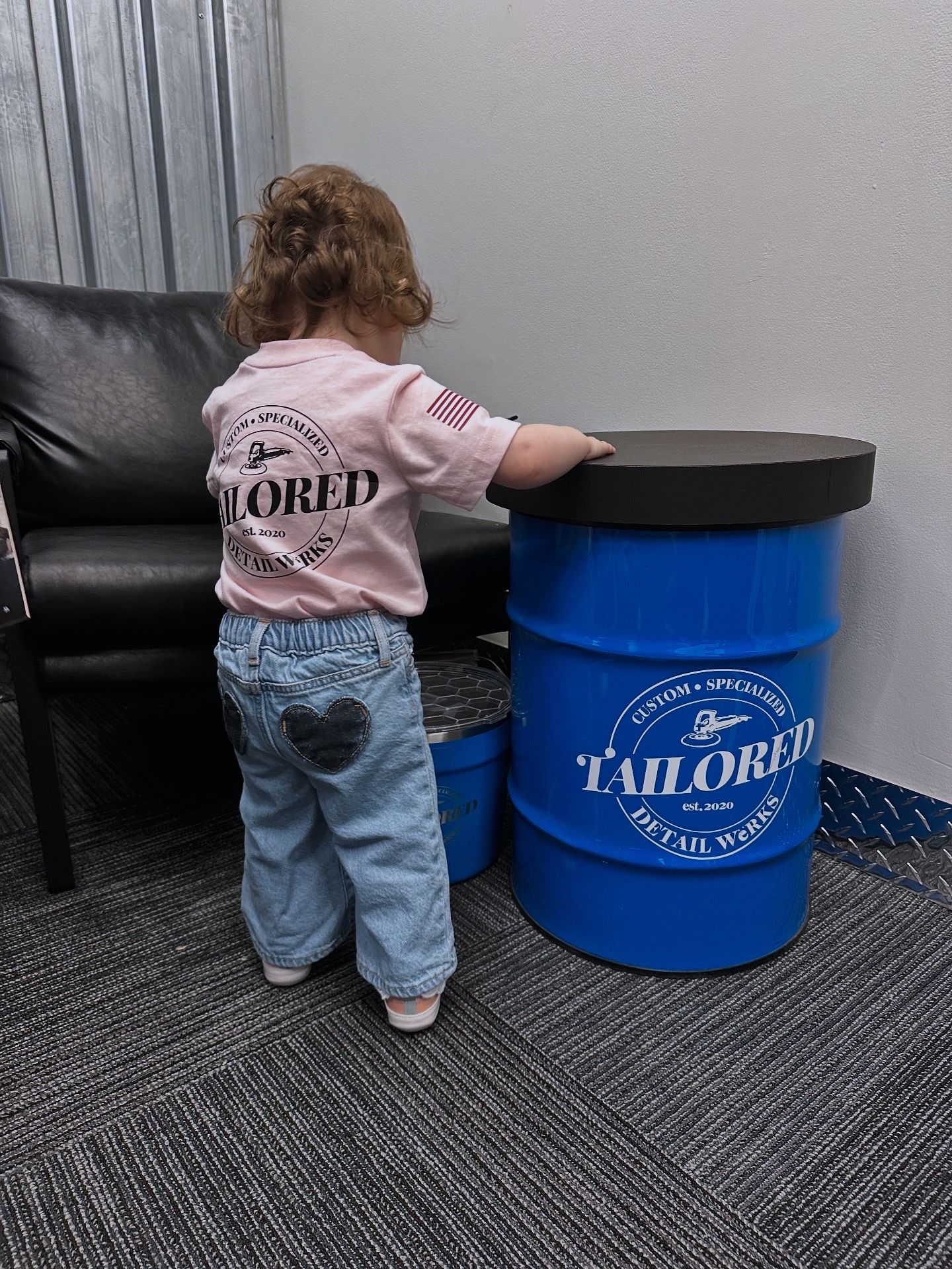 Toddler in pink shirt and jeans standing at a blue barrel table in a carpeted room