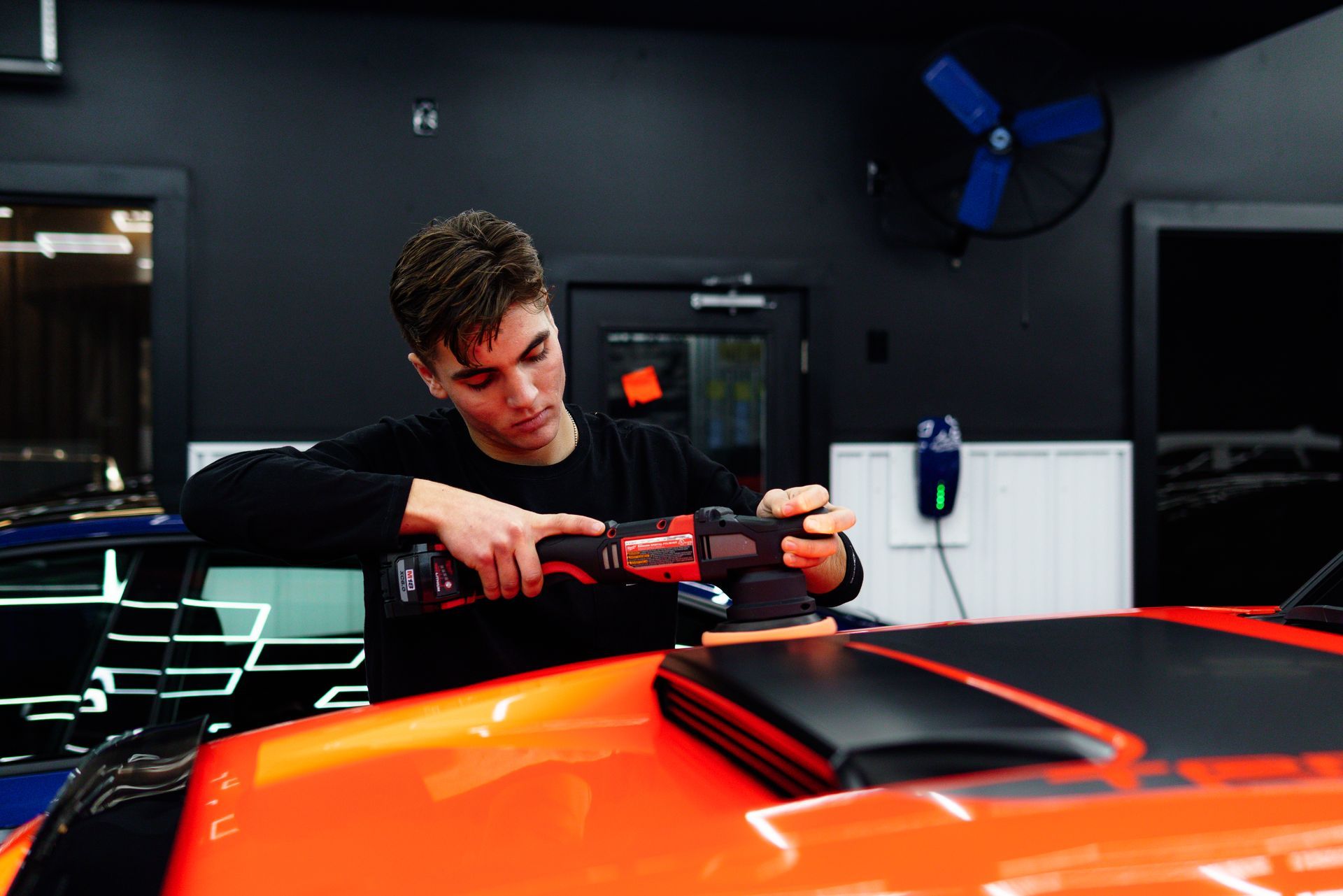 Person polishing a bright orange sports car in a dark garage