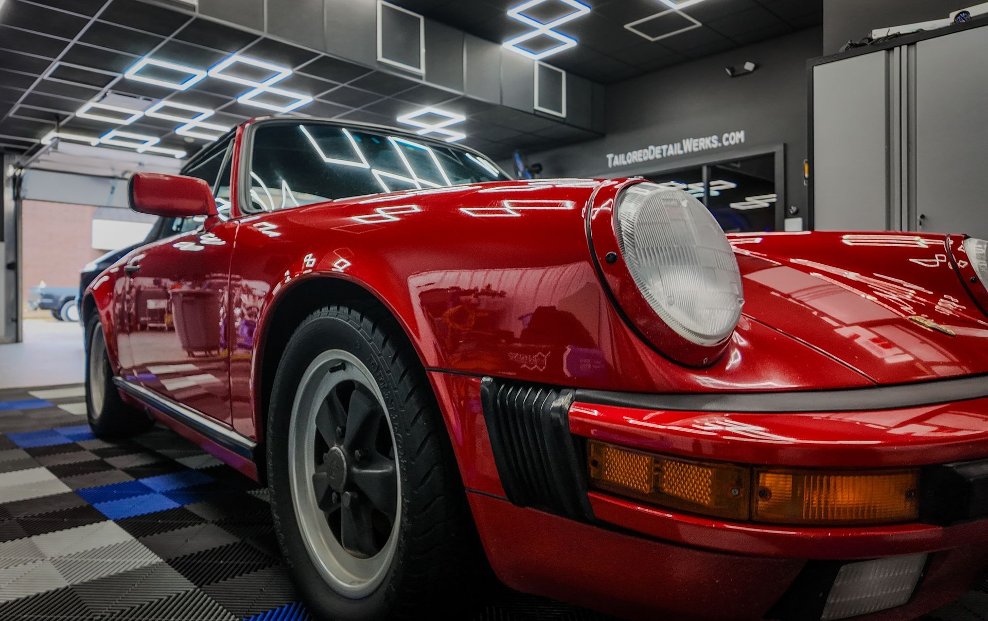 Red classic sports car in a showroom, viewed from the front-left, with glossy paint and round headlights.