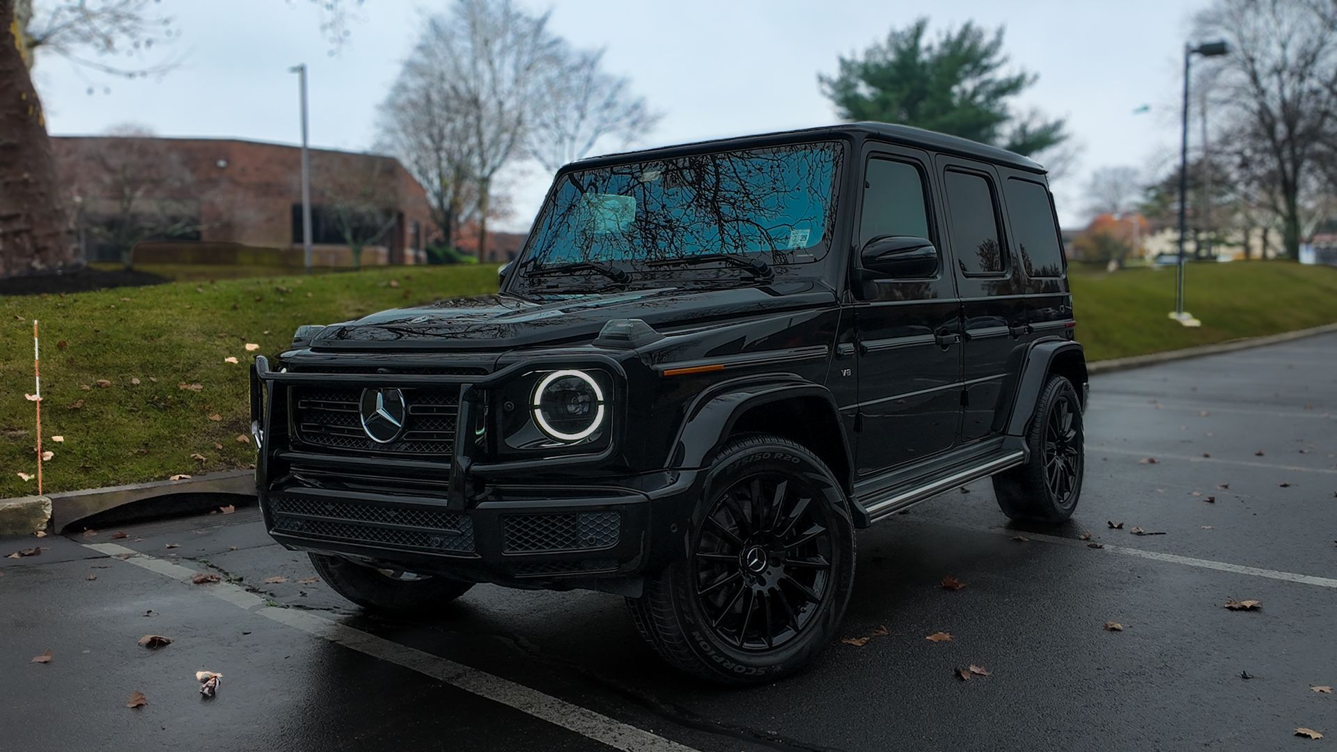 Black SUV parked in a wet lot on a rainy day, with trees and a brick building in the background