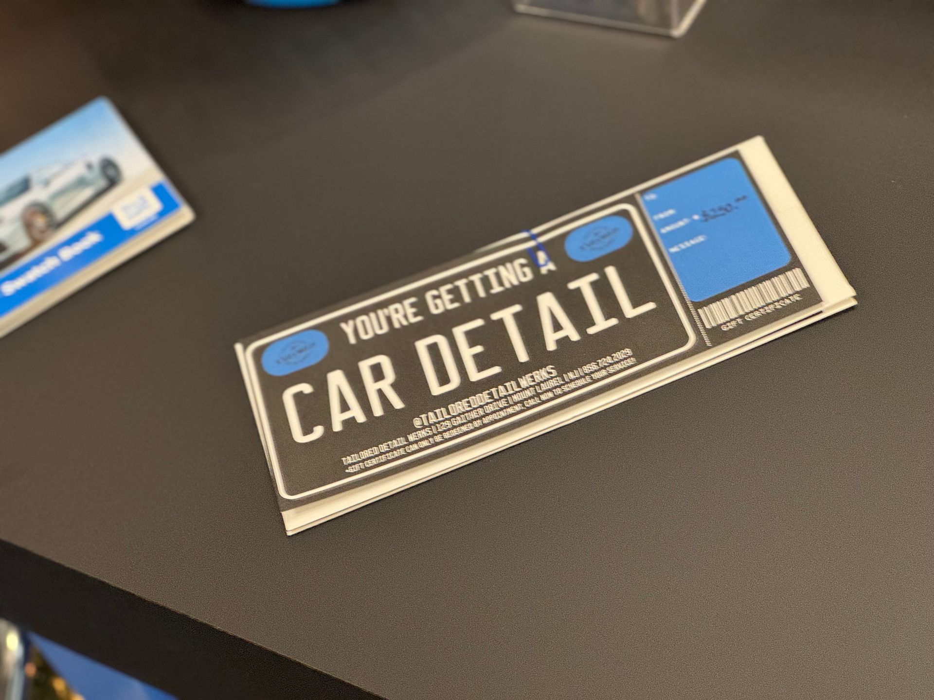 Flyer on a dark table advertising “You’re Getting a Car Detail” with a blue car photo in the corner